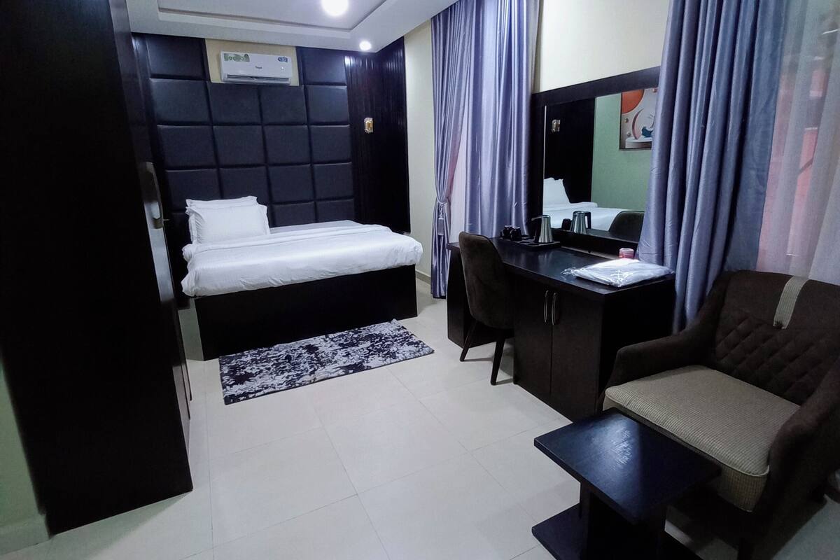 A modern hotel room with a bed, desk, chair, and a small table.