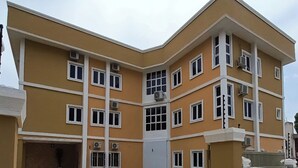 A multi-story building with a yellow facade, multiple windows, and air conditioning units. - Kelvic Systems Apartments (Abuja)