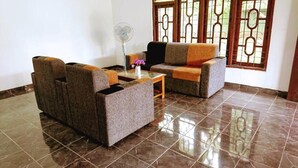 A living room with two sofas, a coffee table, and a fan. - A A A Guest House (Dambulla)
