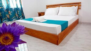A neatly made bed with white and teal bedding, a wooden headboard, and a small wooden nightstand beside it. - A A A Guest House (Dambulla)