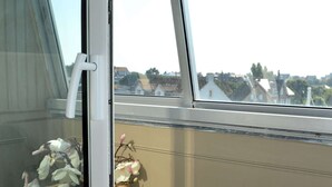 A window with a view of a balcony, a wicker basket, and a white curtain. - L'Escale - Studio with loggia in the city center (Courseulles-sur-Mer)
