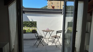 Un balcon avec une table et deux chaises, une vue sur un immeuble et une clôture.
