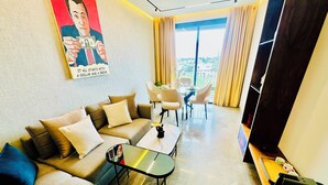 A modern living room with a sofa, coffee table, and dining area. There is a poster on the wall and a large window with curtains. - Stay'Inn - Rafina Sunset (Casablanca)