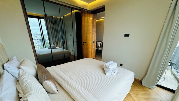 A hotel room with a large bed, a wardrobe, a bathroom, and a view of the city. - Stay'Inn - Rafina Sunset (Casablanca)