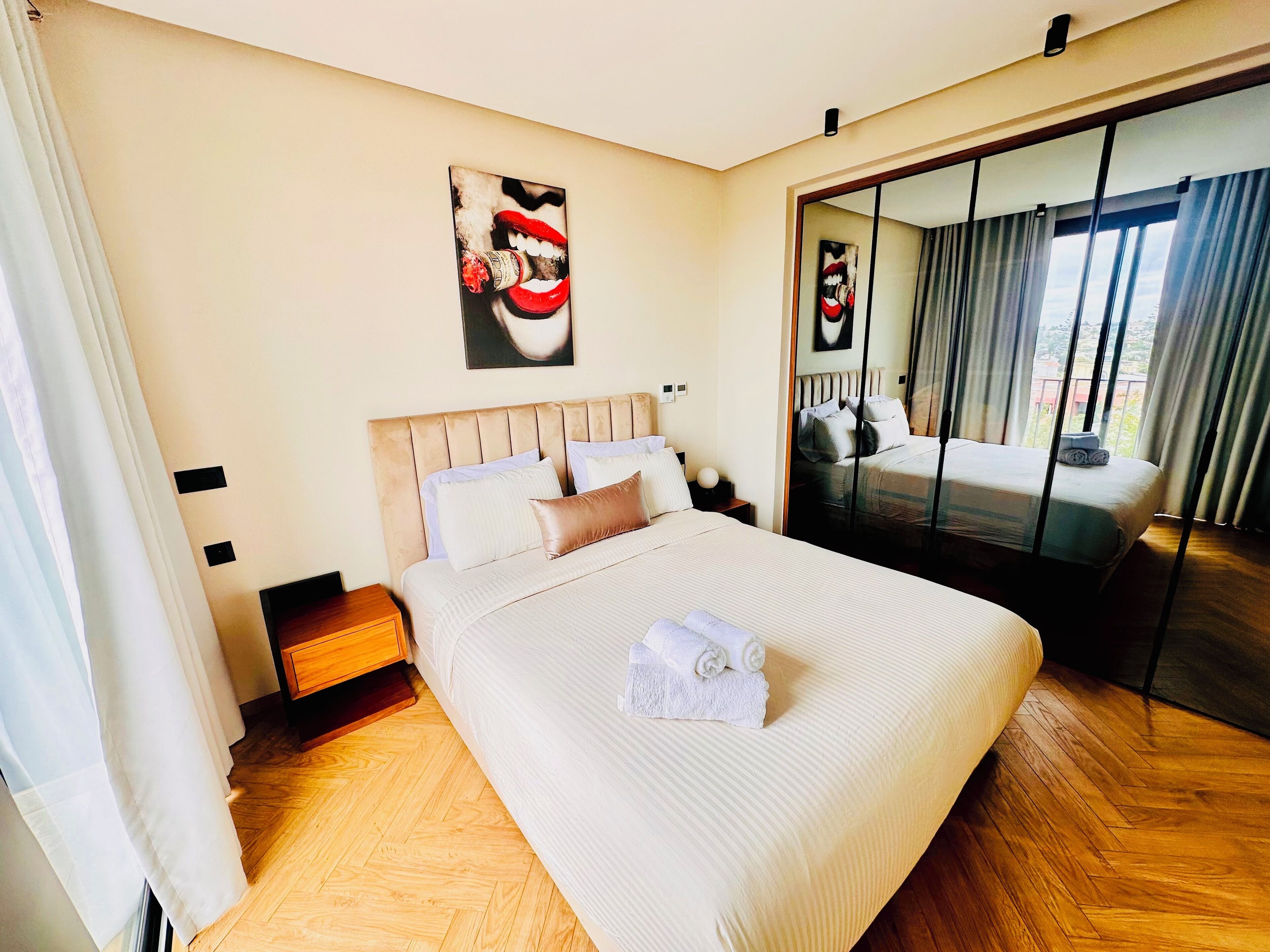 Una camera d'albergo con un letto grande, un pavimento in legno, un comodino, uno specchio e un quadro appeso al muro.