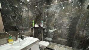 A modern bathroom with a marble sink, toilet, and shower area.