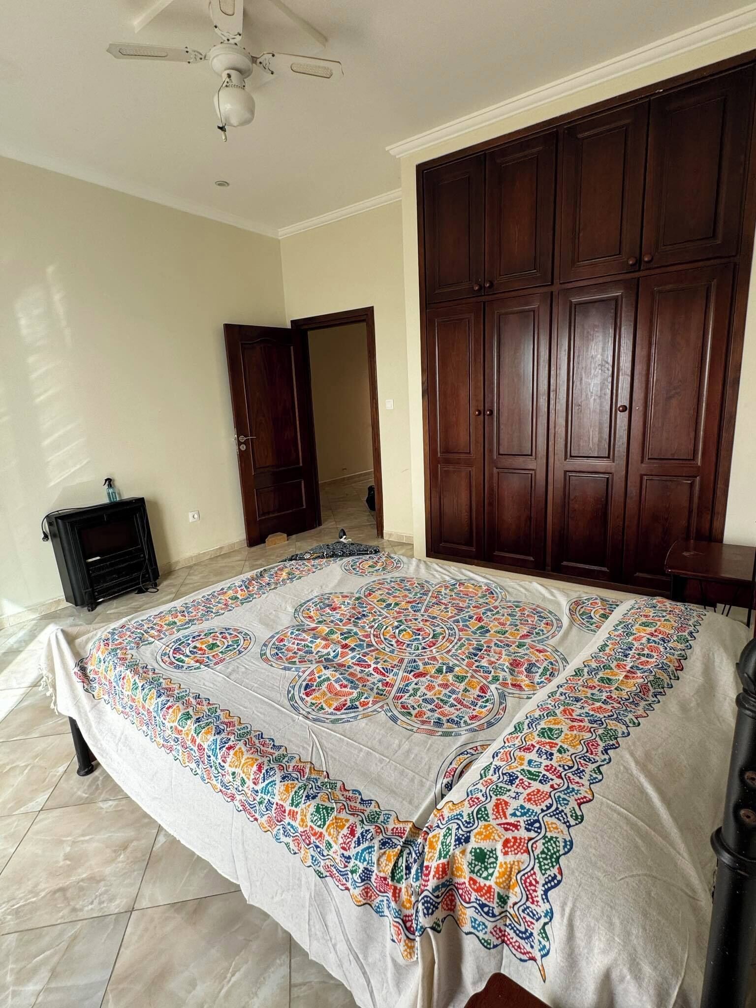 Een slaapkamer met een groot bed, een houten garderobe, een plafondventilator en een zwarte kast.
