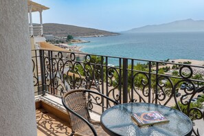 A balcony with a view of the sea, a round table, and a wicker chair.