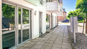A modern building with large glass doors and windows, a tiled walkway, and a parked car in the background.