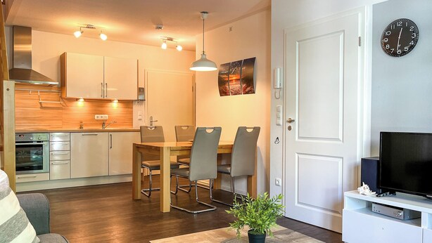 A modern apartment with a dining area, kitchen, living room, and a TV.