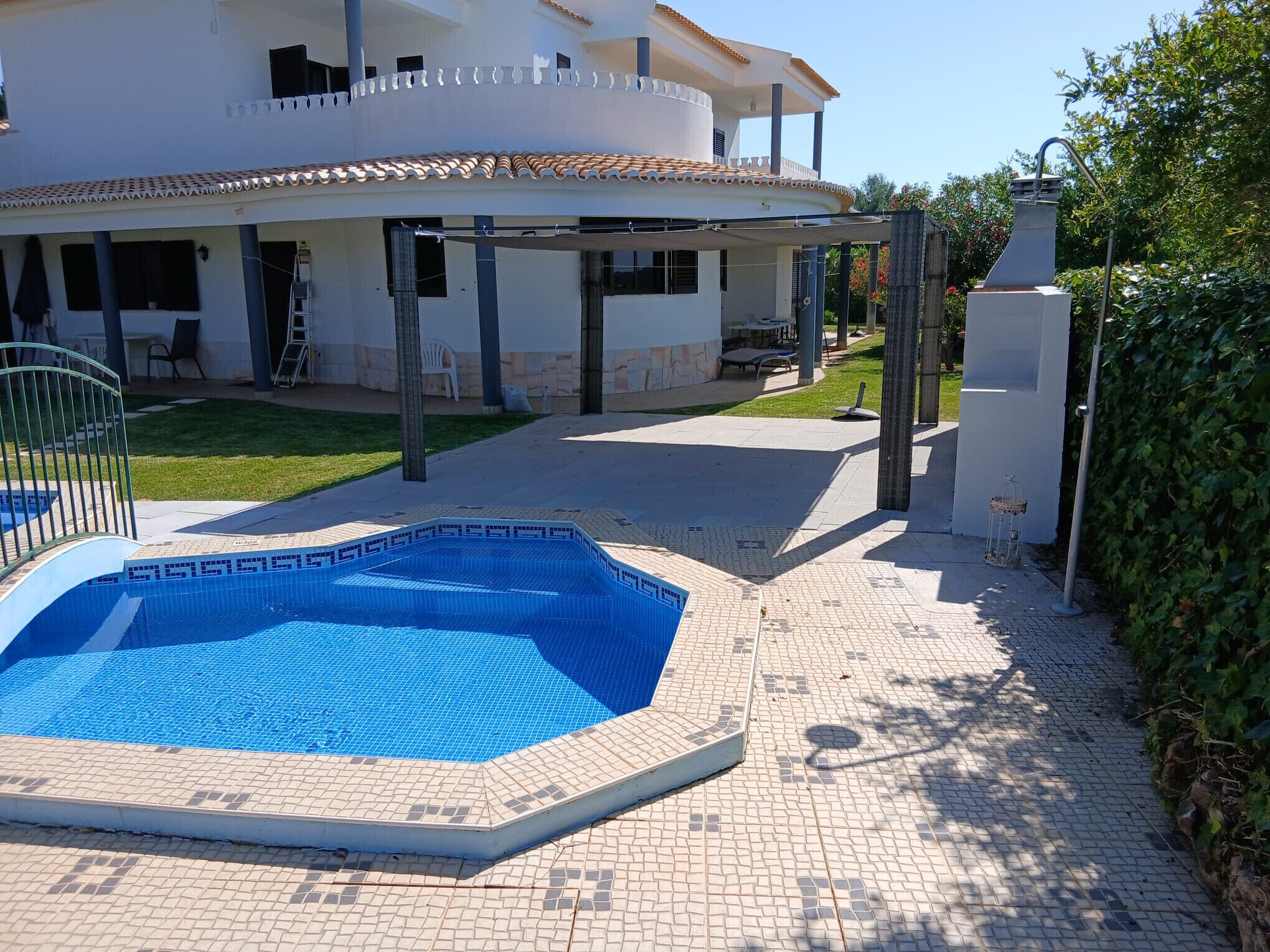 Una piscina con un borde empedrado, un patio cubierto y un edificio con techo de tejas.