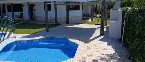 A swimming pool with a tiled deck, a covered patio area, and a building with a tiled roof.
