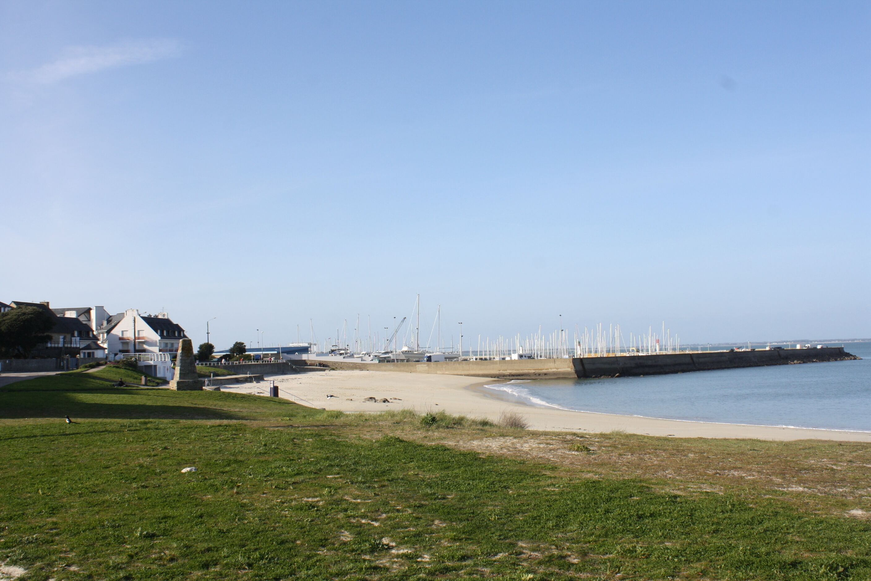A coastal area with a sandy beach, grassy areas, and a pier with boats.