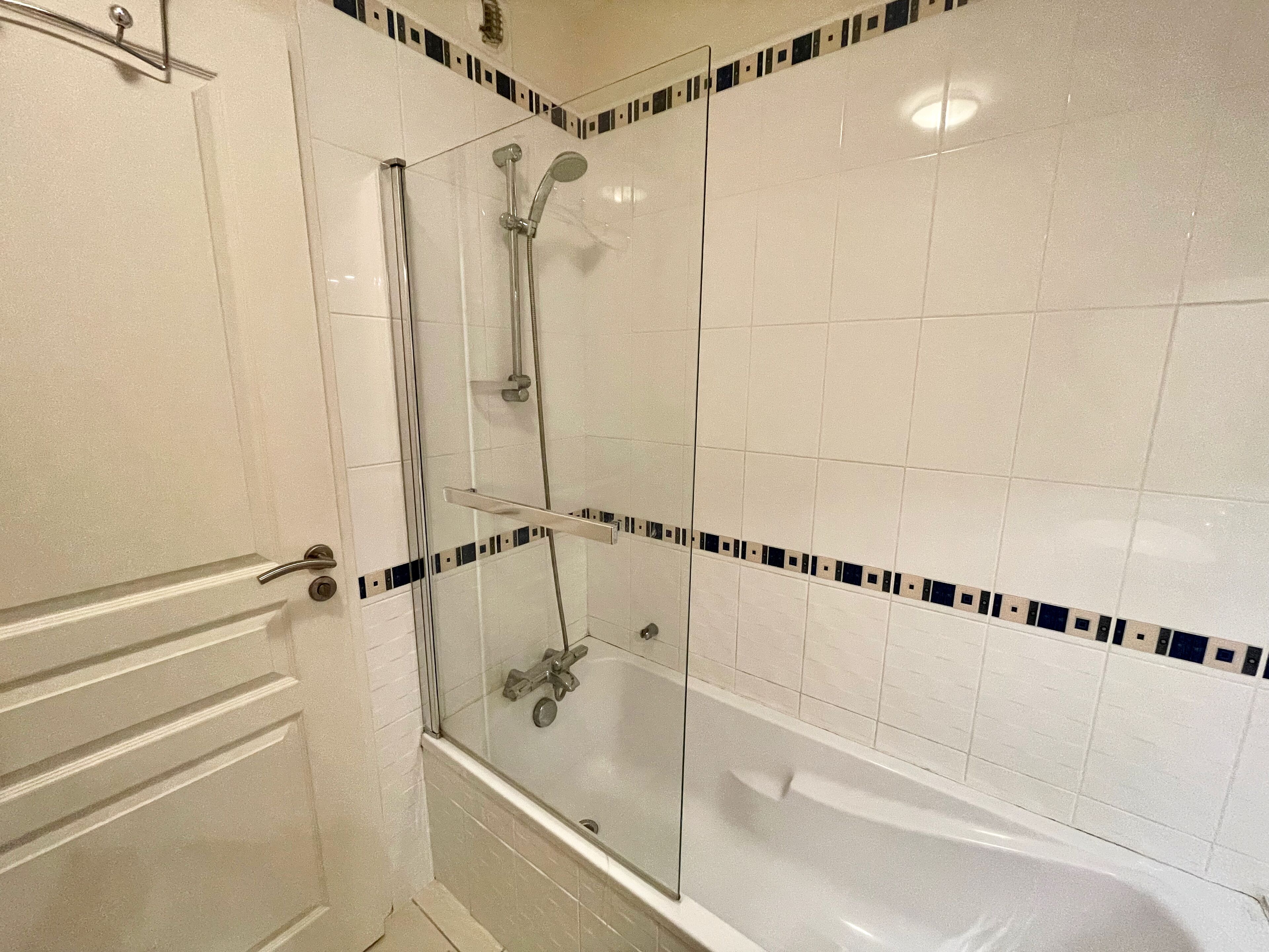 A bathroom with a glass-enclosed shower, a bathtub, and a door with a handle.