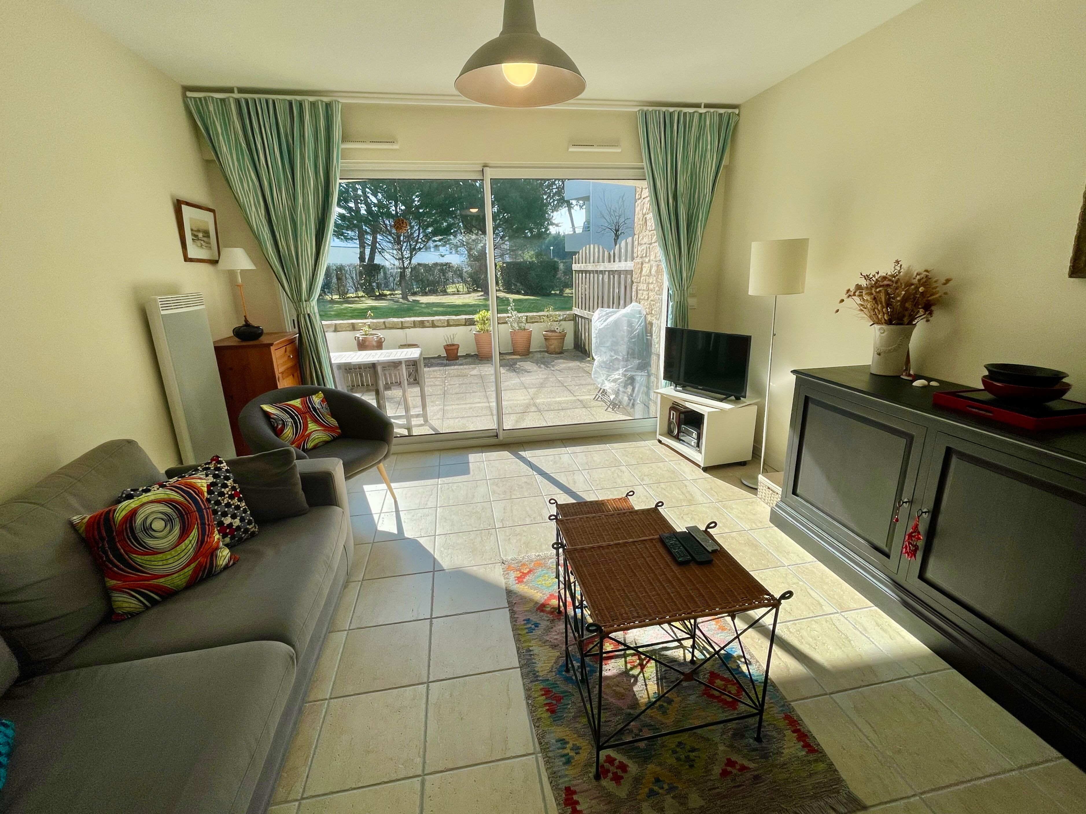 A living room with a sofa, TV, and a view of a garden through a sliding glass door.