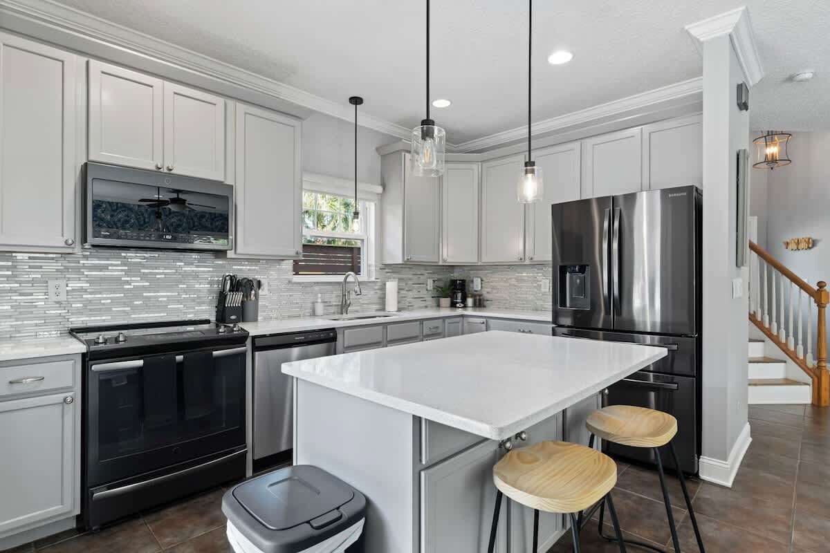 A modern kitchen with white cabinetry, stainless steel appliances, a large island, and pendant lighting.