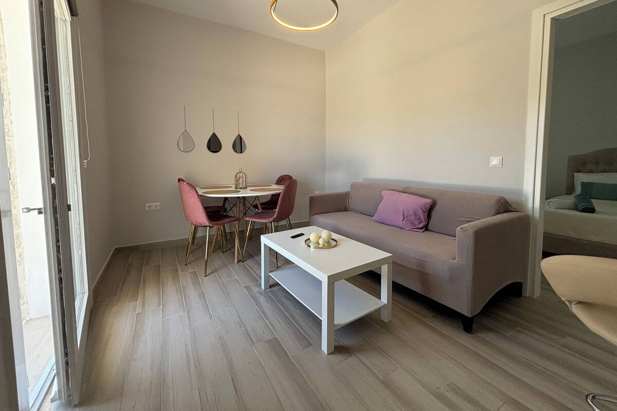 Ein modernes Wohnzimmer mit einer Couch, einem Couchtisch, einem Esstisch mit Stühlen und Pendelleuchten.
