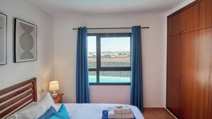 A bedroom with a bed, a nightstand with a lamp, a window with curtains, and a wardrobe.