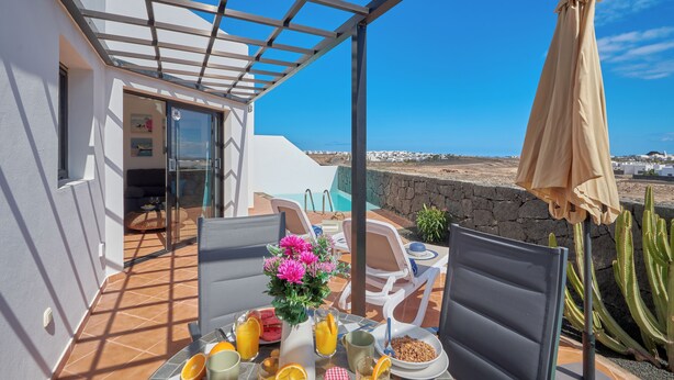 A patio with a table set for breakfast, a glass door leading to a pool, and a view of the sea.
