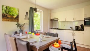 Une cuisine moderne avec des meubles blancs, une table à manger dressée avec des assiettes, des tasses et un vase rempli de fleurs.
