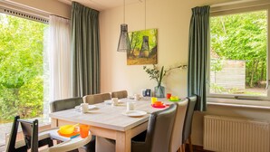 Un espace repas avec une table en bois, des chaises et une vue sur la verdure à l’extérieur.