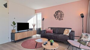 A modern living room with a flat-screen TV, a dark grey sofa, a wooden coffee table, and a red rug. - Semi-detached bungalow for 5 persons (Vlagtwedde)