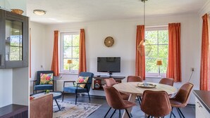 A modern living room with a dining area, large windows with curtains, a flat-screen TV, and a fireplace. - Detached 6-person bungalow (Vlagtwedde)
