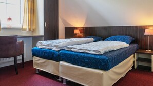 A double bed with blue bedding, a bedside table with a lamp, a chair, and a window with curtains. - Detached 6-person bungalow (Vlagtwedde)