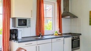 A compact kitchen with white cabinets, a microwave, a coffee maker, a sink, and a stove. - Detached 6-person bungalow (Vlagtwedde)