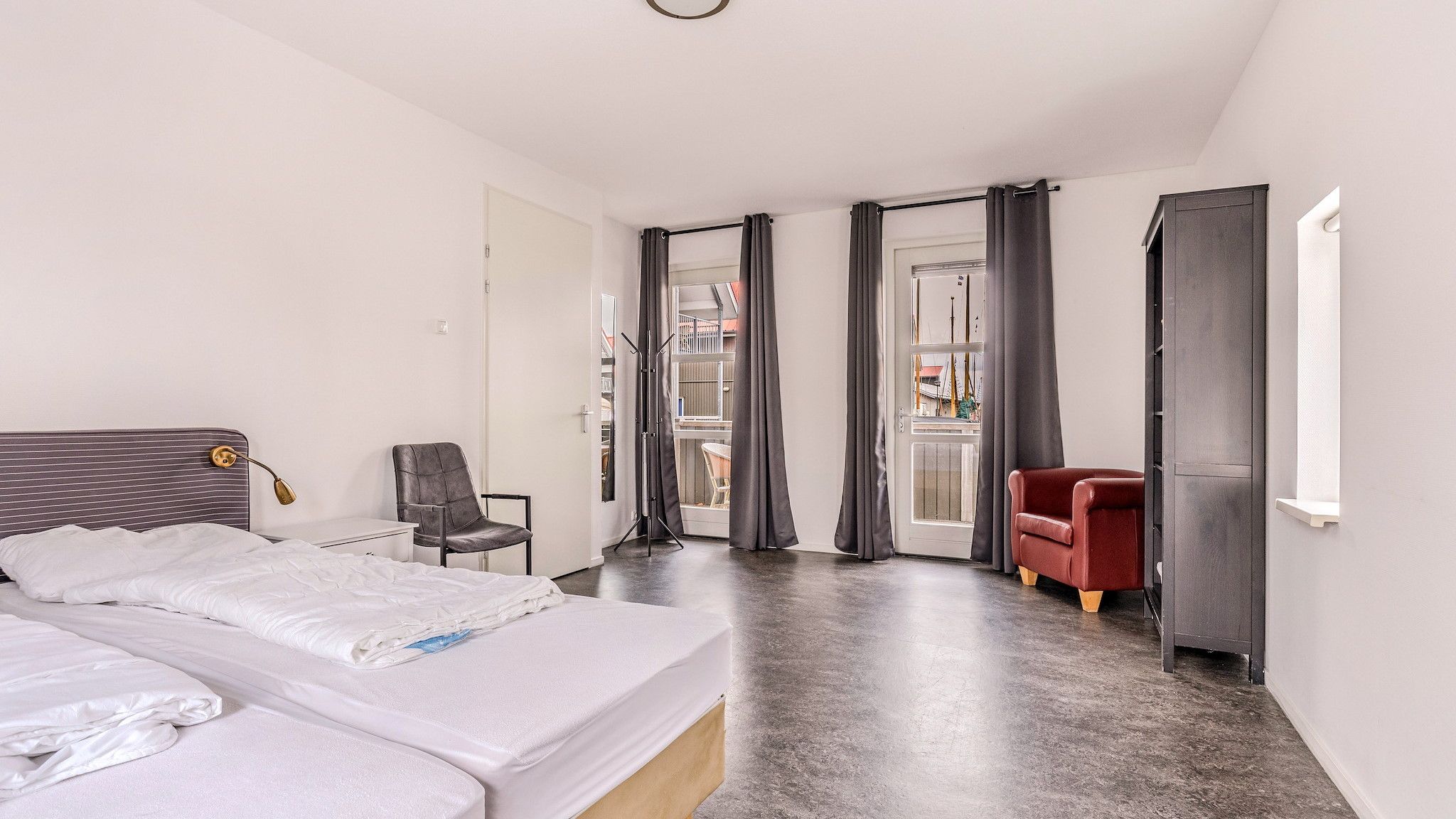 A hotel room with a bed, a chair, a desk, and a window with curtains.