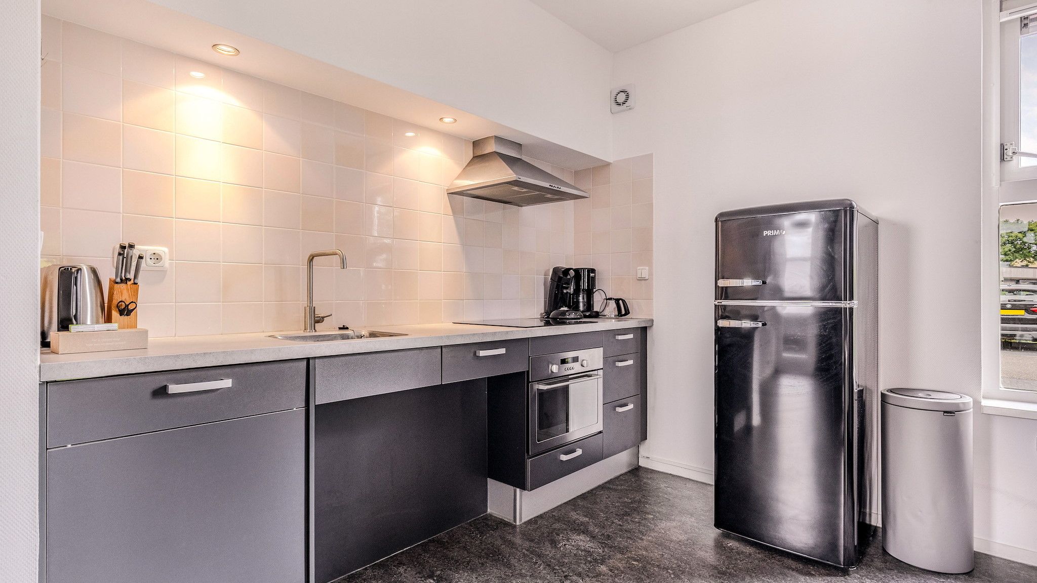 A modern kitchen with a stainless steel refrigerator, a coffee maker, and a built-in oven.