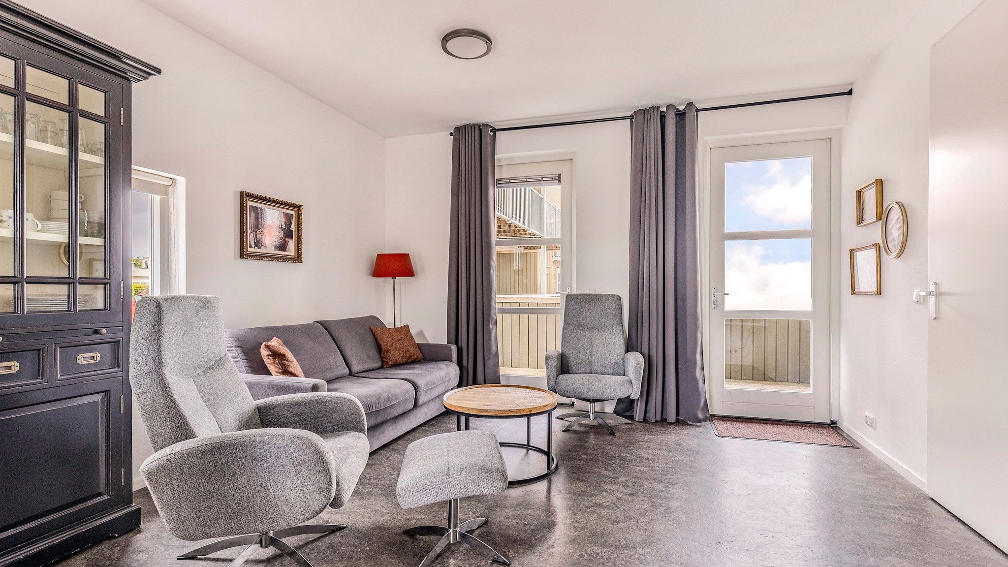 A modern living room with a grey sofa, two armchairs, a small round table, and a cabinet.