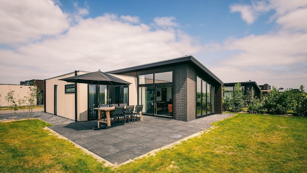 Ein modernes Haus mit einer Terrassenfläche, einem Esstisch und Stühlen.
