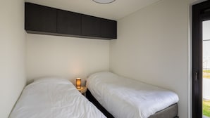 Ein kleines, gemütliches Zimmer mit zwei Einzelbetten, einem Nachttisch mit Lampe und einem dunklen Schrank über den Betten.