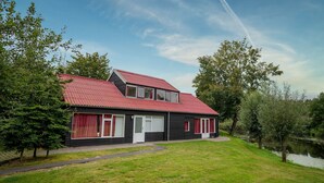 Et toetagers hus med rødt tag, en lille veranda og en sø i baggrunden.