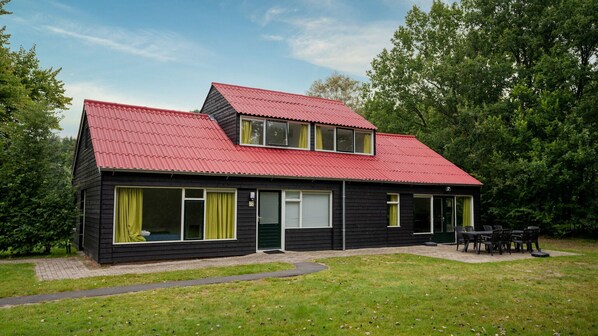 A two-story house with a red roof, black siding, and a small porch with outdoor seating.