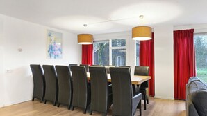 Et spiseområde med et bord og stole, store vinduer med røde gardiner og en hængende lampe.