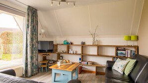A cozy living room with a TV, wooden shelves, a sofa, and a window with curtains.
