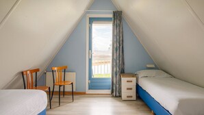 A small, triangular attic bedroom with a single bed, a chair, a small table, and a window with curtains.