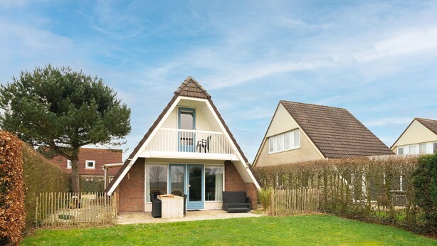 A two-story house with a balcony, a front door, and a small patio area with outdoor furniture.