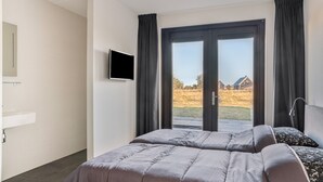 Une chambre d’hôtel avec un lit, une télévision, une salle de bain et une vue sur les maisons depuis la fenêtre.