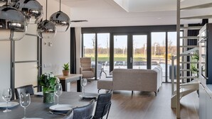 Un espace de repas moderne avec une table dressée pour deux personnes, un canapé et une vue sur une rivière, visible à travers de grandes fenêtres.