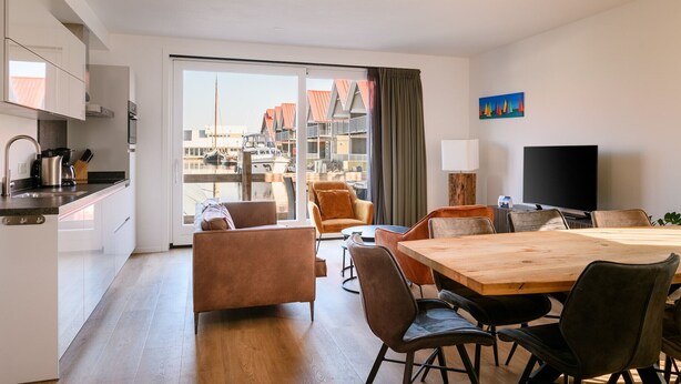 Une chambre d’hôtel moderne dotée d’une cuisine, d’un coin repas et d’une grande fenêtre donnant sur un port de plaisance.