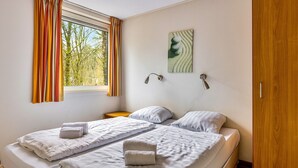 Quarto com duas camas de solteiro, janela com cortinas, luminária de cabeceira e uma obra de arte na parede.