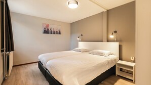 Une chambre bien rangée, avec un grand lit, des tables de chevet et un luminaire fixé au mur.