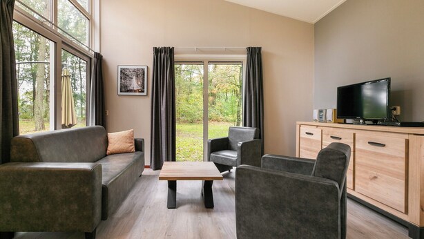 Un salon moderne avec un canapé, des fauteuils, une table basse et un téléviseur posé sur un meuble en bois.