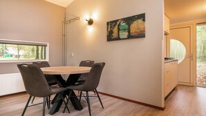 Un coin repas avec une table ronde et six chaises, un tableau au mur et une fenêtre donnant sur les arbres.