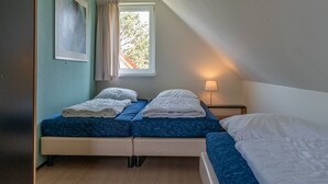A bedroom with two beds, a window with curtains, a bedside table with a lamp, and a framed picture on the wall. - Detached bungalow for 8 persons (Vlagtwedde)