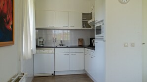 A compact kitchen with white cabinets, a dishwasher, a microwave, and a coffee maker. - Detached bungalow for 8 persons (Vlagtwedde)
