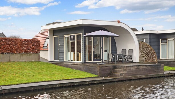 Une maison moderne dotée d’un patio couvert, d’un canal d’eau à l’avant et d’une pelouse verdoyante.